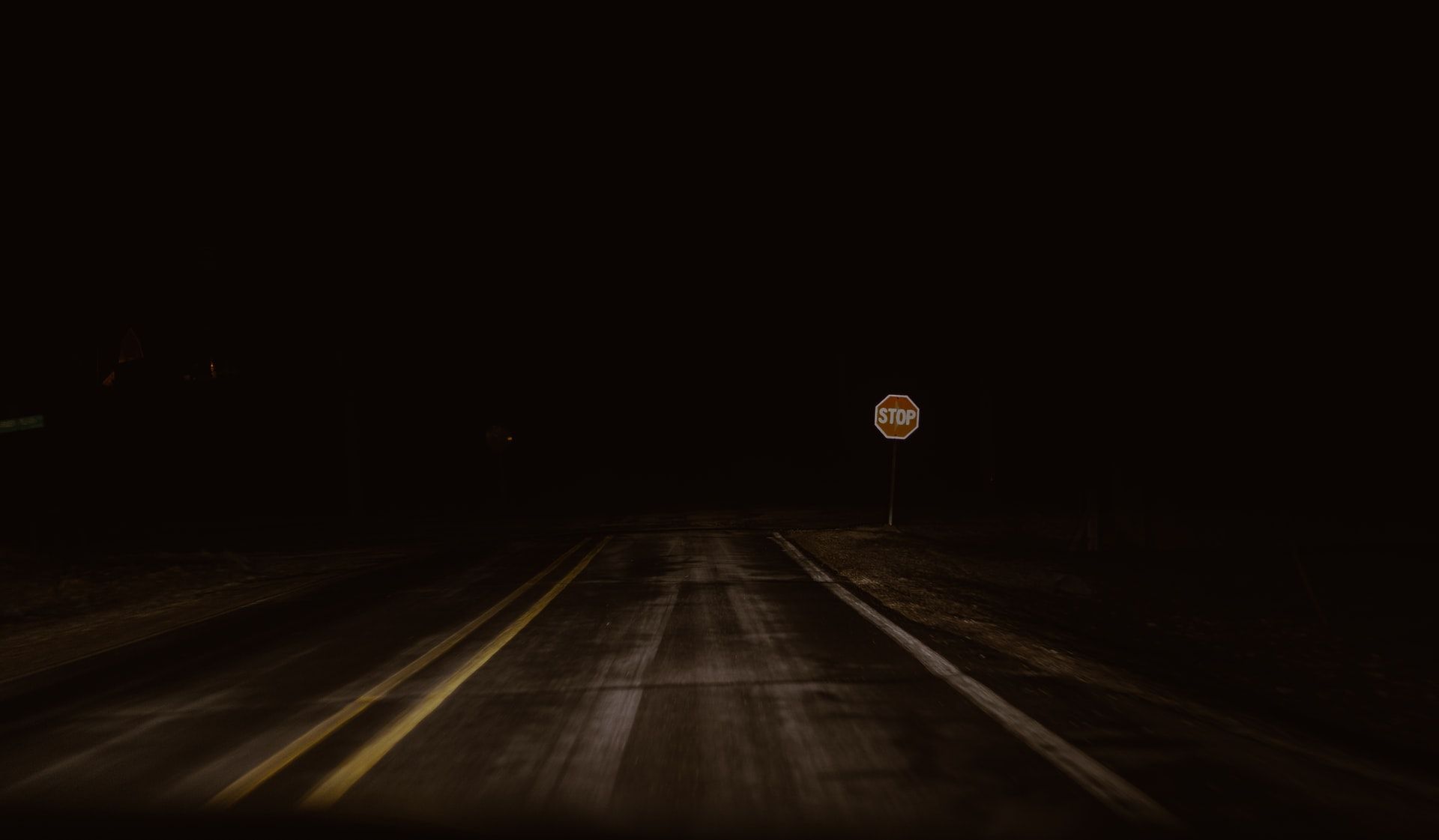 Road in the dark with poor lighting, a stop sign just visible in the distance