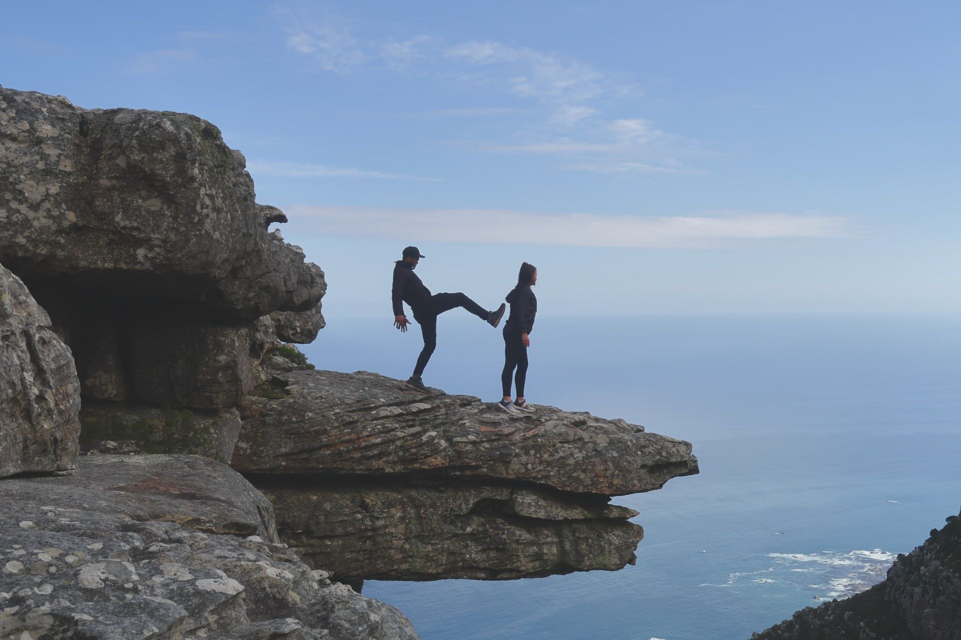 Table Mountain (Nature Reserve), Cape Town, South Africa . On a table of rock overlooking a valley, a man faces a woman with one leg up as if he is about to kick her off. She faces the valley.