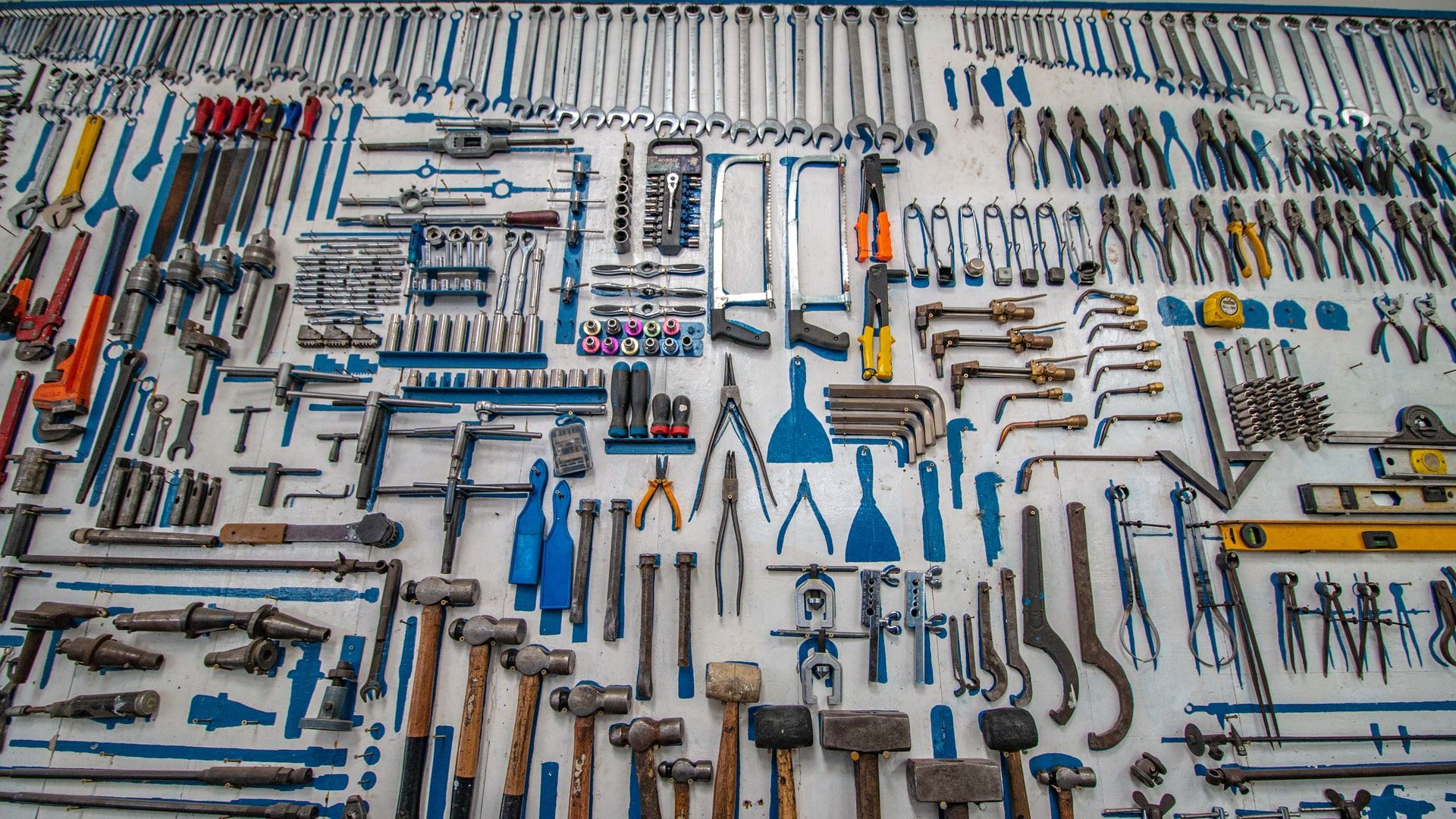 A large number of tools hanging on pegs in a wall. The tools are all hand tools and very near to one another.